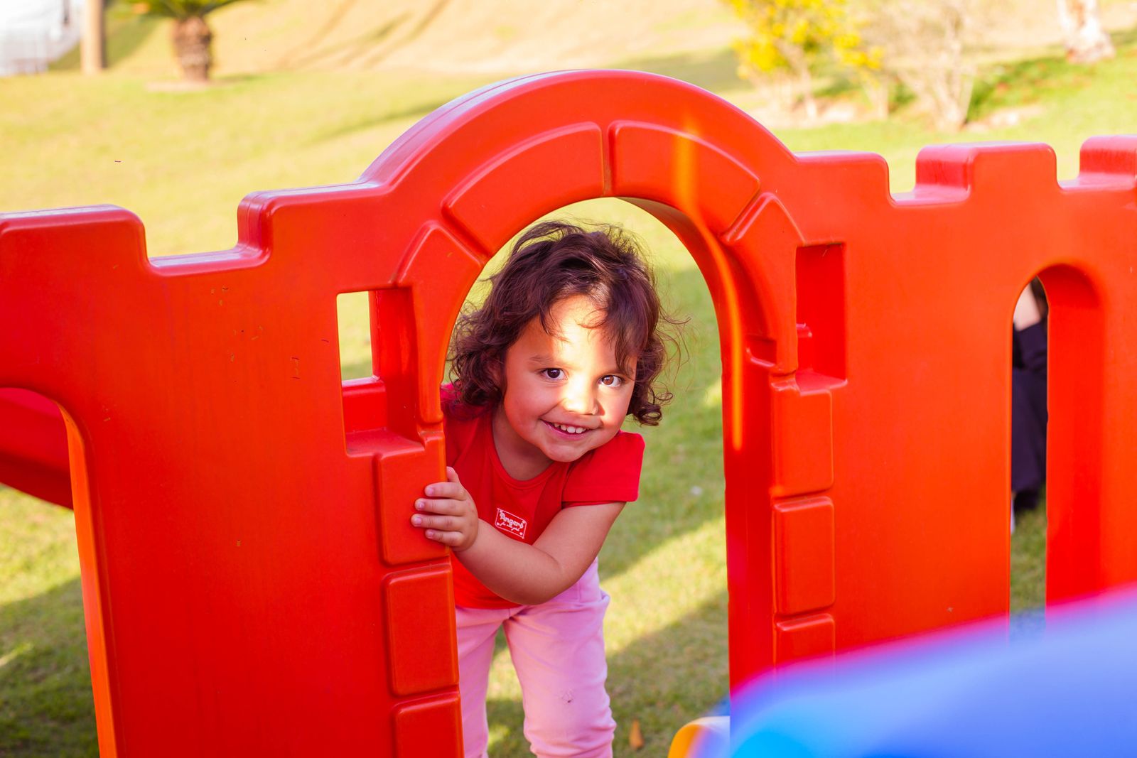 Menina sorrindo enquanto brinca na casinha colorida do parque do Colégio